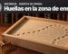 Ilustración con una metáfora visual: en una biblioteca de lomos de cuero, una caja de arena de madera clara rastrillada, cruzada por huellas mecánicas diminutas que dan una vuelta sin salir de la caja; adelante, un pequeño rastrillo de bronce. Arriba, en una franja oscura, el logo de Wikipedia, el texto «Wikimedia · Agentes de OpenAI» y el titular «Huellas en la zona de ensayo».